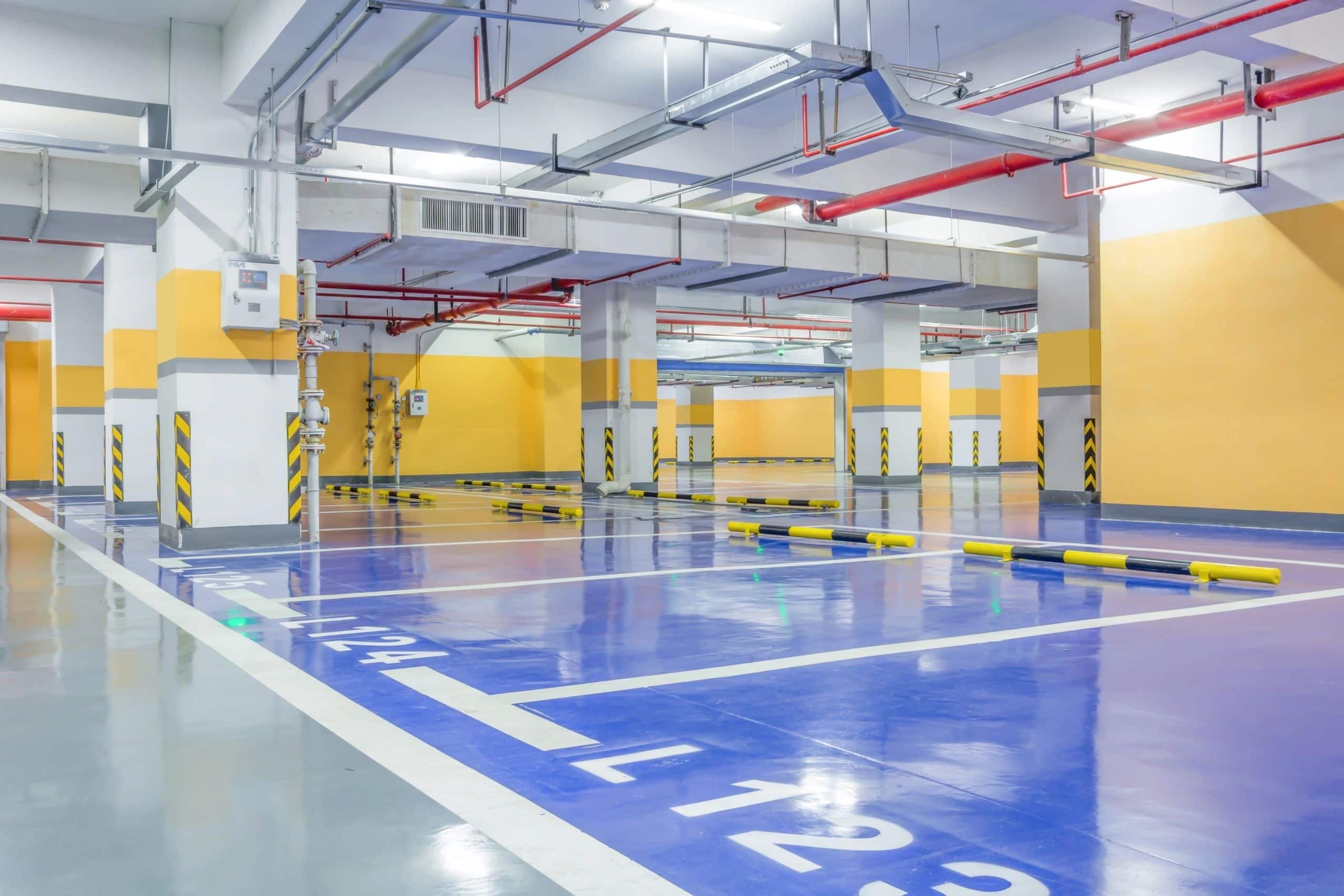 Tiefgarage mit blau beschichteten Stellplätzen, weißen Markierungen und gelben Anfahrschutzbügeln