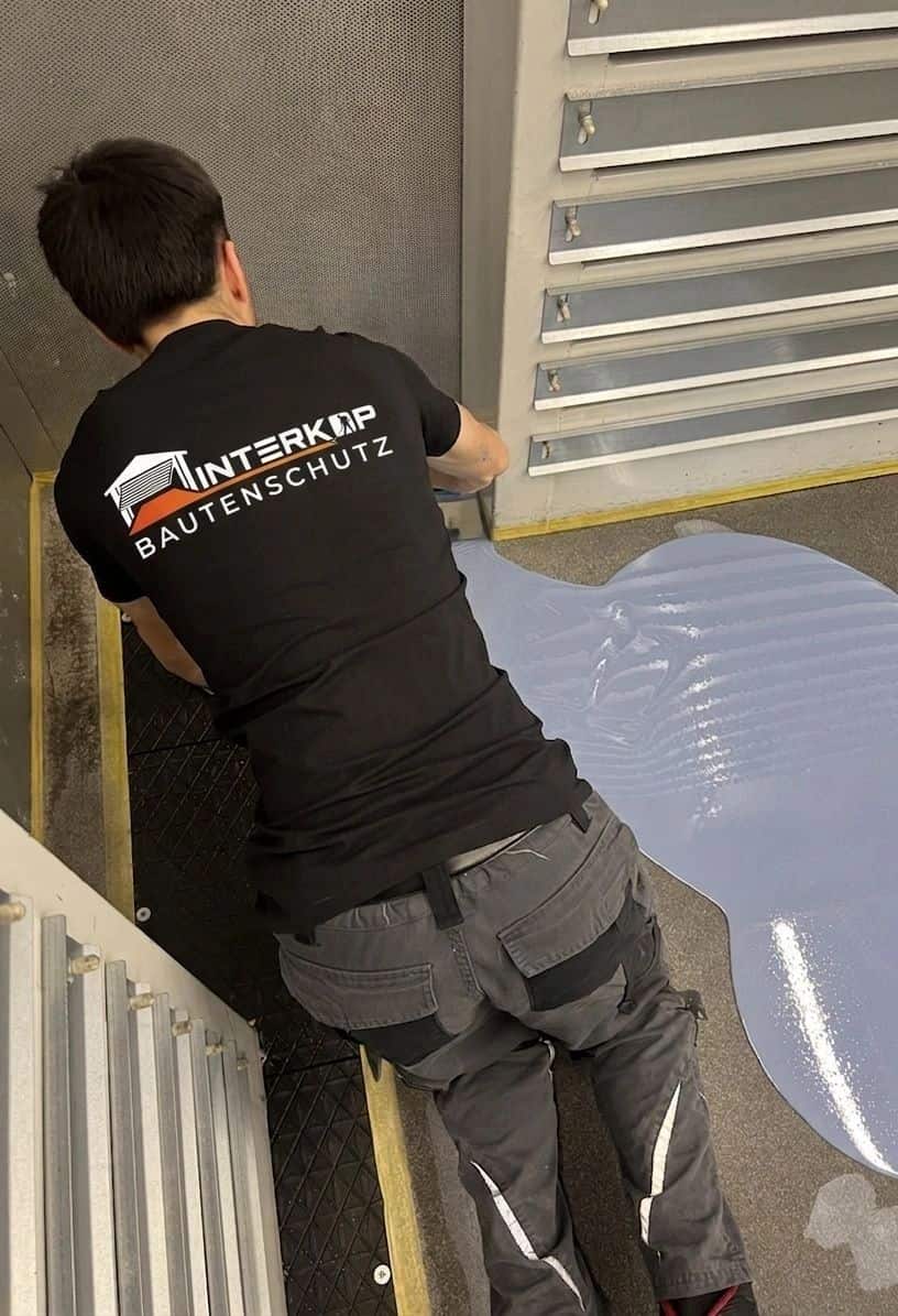 Mitarbeiter im Interkop-Shirt verteilt frisch gegossenes, blaugraues Harz mit der Kelle an einer Kante